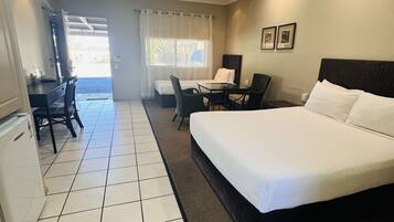 A hotel room with a large bed, a desk with a chair, a small table, and a refrigerator.