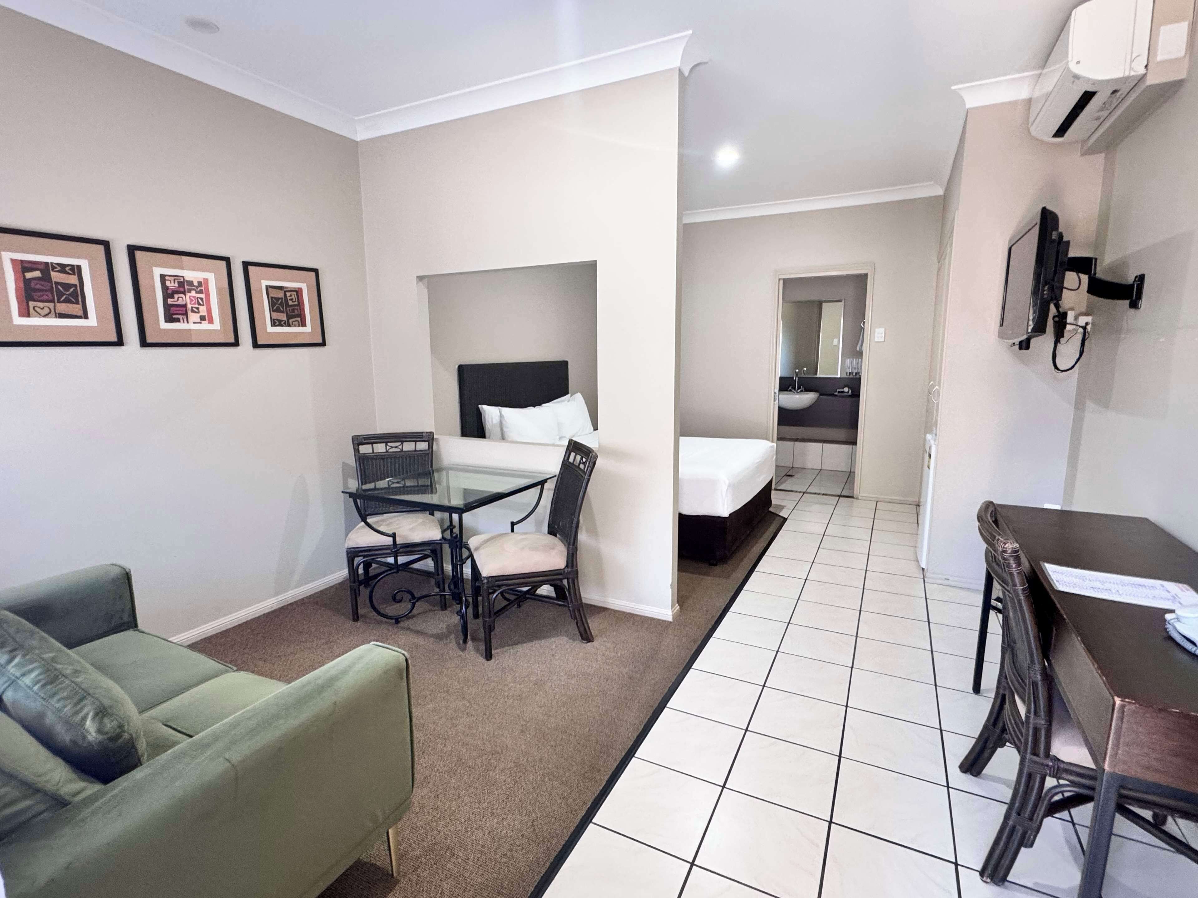A hotel room with a bed, a small table with chairs, a green sofa, and a bathroom visible through an open door.