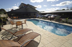 A swimming pool with lounge chairs, a covered patio area, and a building with a sign.