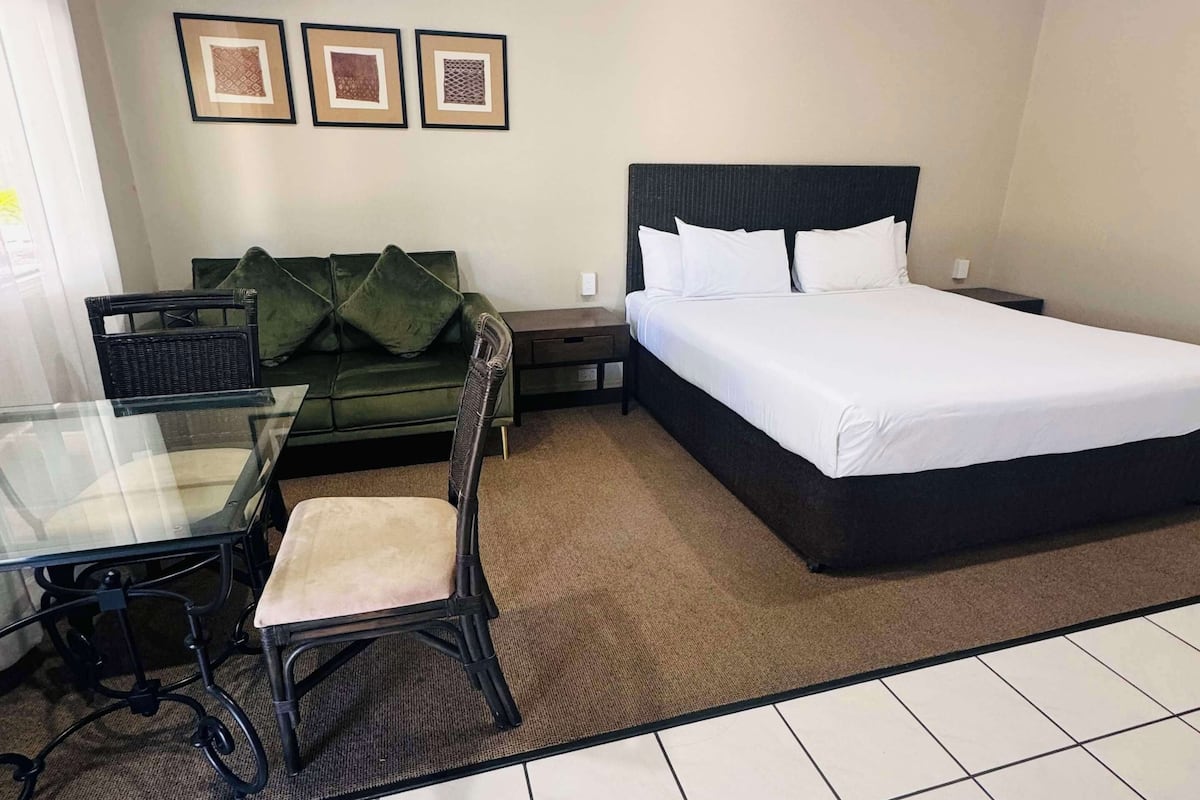 Habitación de hotel con cama, sof á, una mesita y una silla. En la pared, tres cuadros enmarcados.