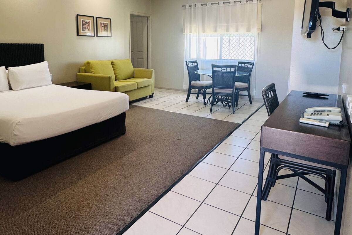 A hotel room with a bed, a sofa, a dining table with chairs, a TV, and a window with curtains.