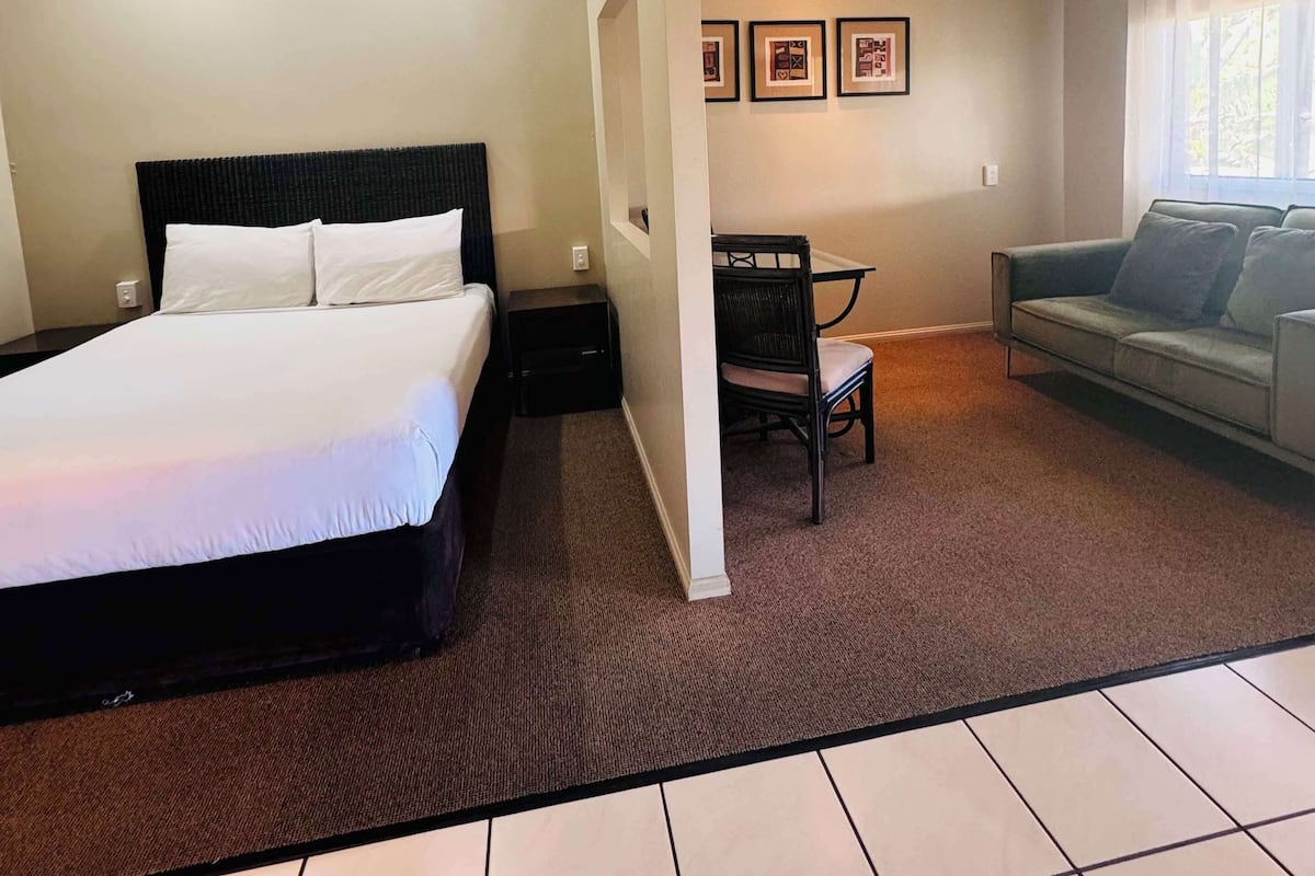 Habitación de hotel con una cama grande, un escritorio, una silla, un sofá y cuadros en la pared.