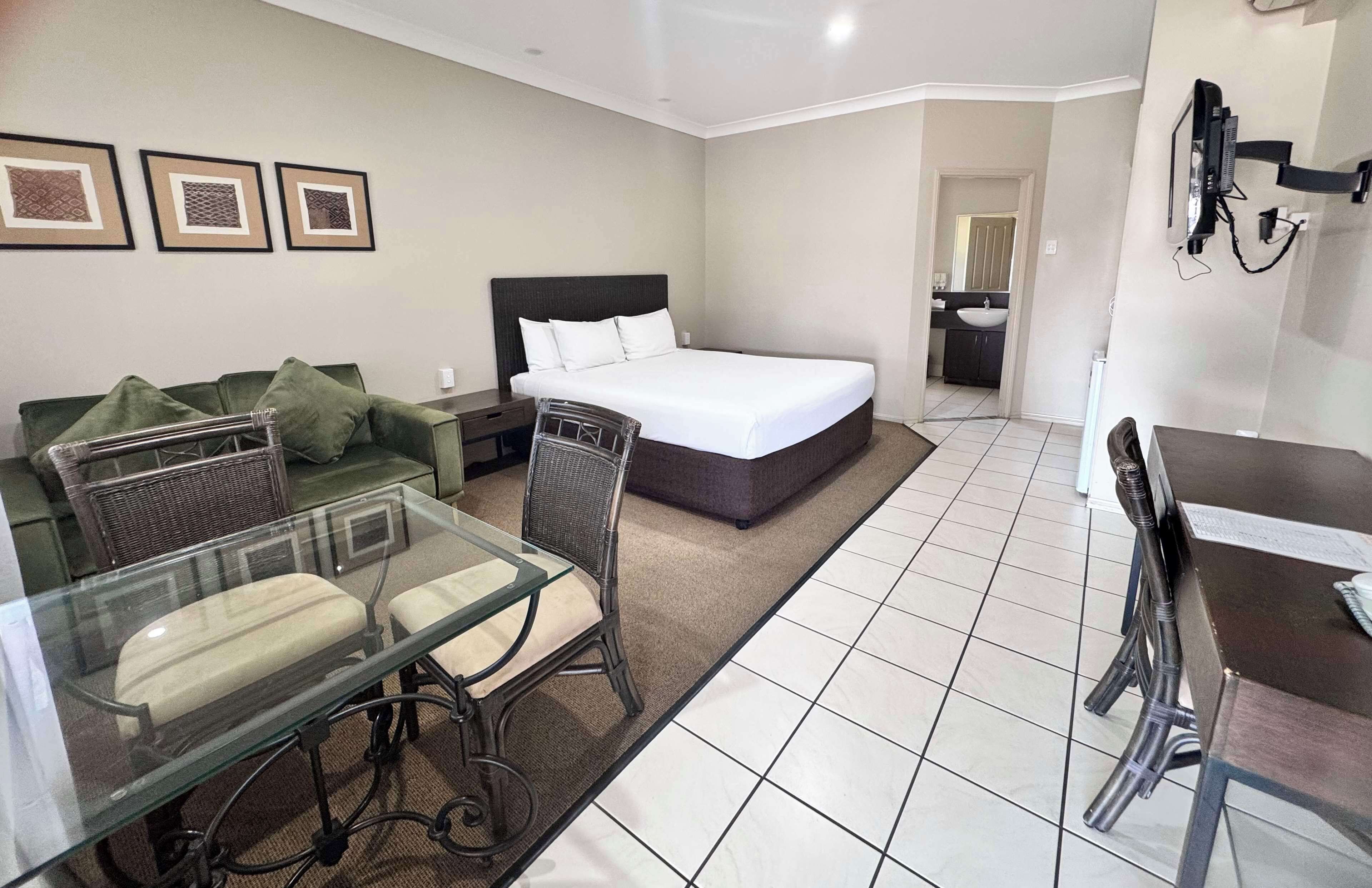 Une chambre d’hôtel compacte comprenant un lit, une table à manger en verre, un canapé et une petite kitchenette.