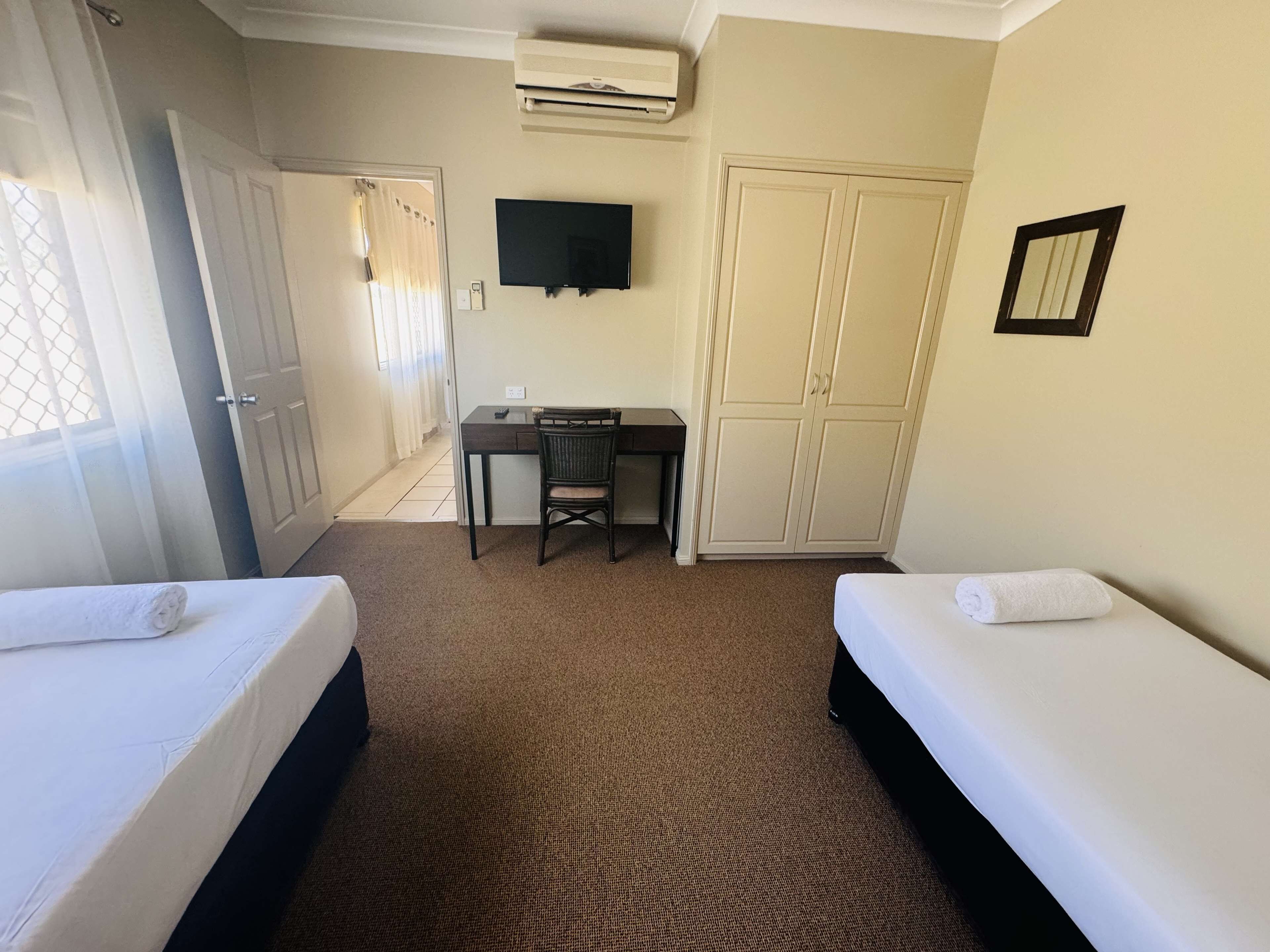 Habitación de hotel con dos camas, un escritorio, una silla, un televisor y un armario.