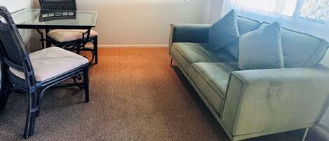 Una sala de estar con una mesa de vidrio, dos sillas, un sofá y tres cuadros en la pared.