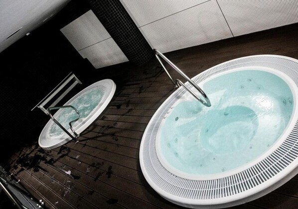 Un jacuzzi con una escalera metálica, un recipiente más pequeño y una cubierta de madera.