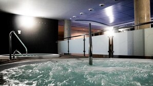 A hot tub in a modern indoor setting with a tiled wall and ceiling lights.