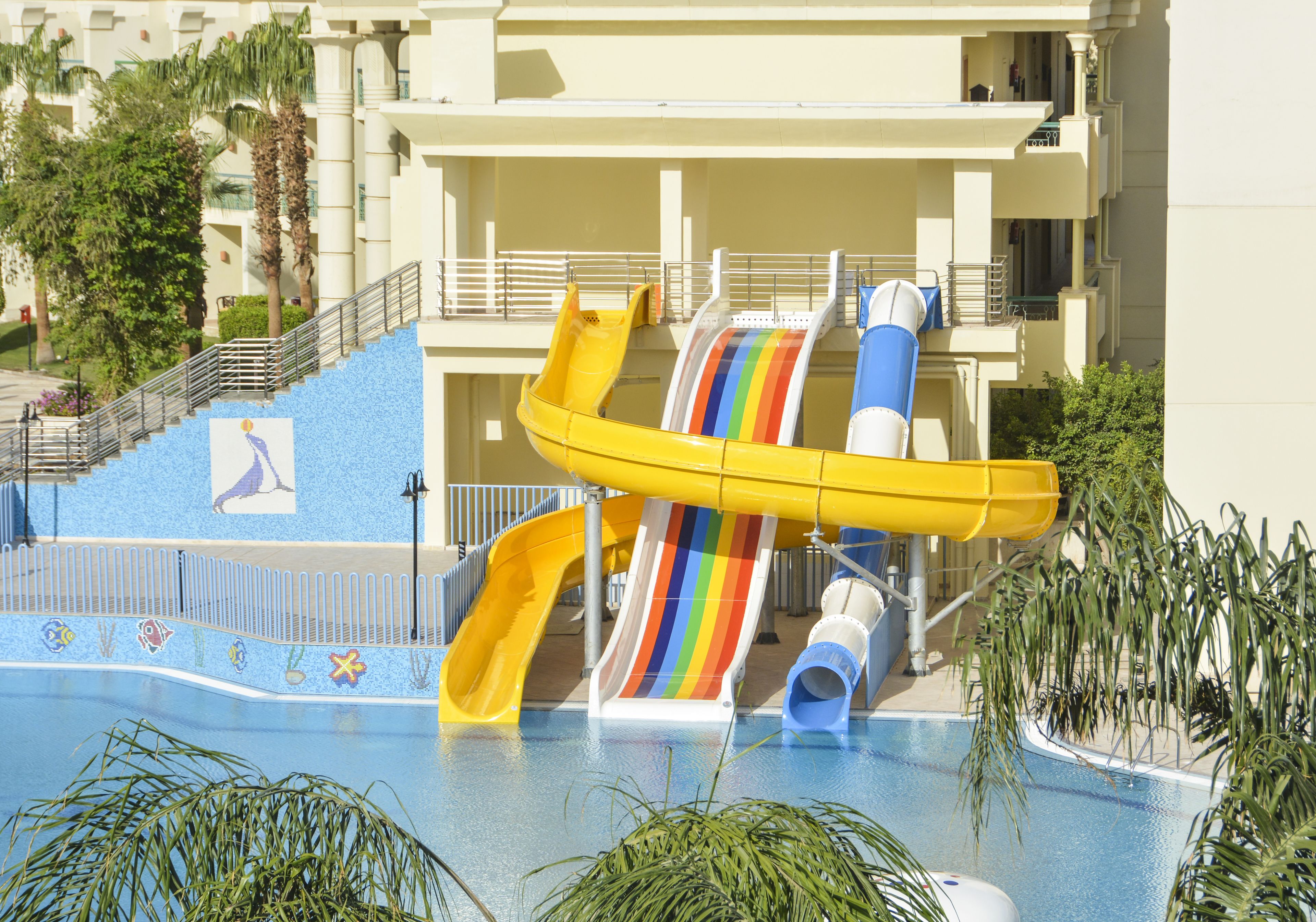 Una piscina con múltiples toboganes, una escalera y un edificio con balcones.