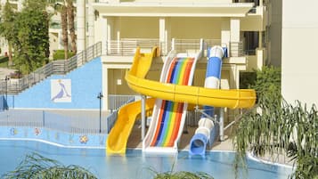 Una piscina con múltiples toboganes, una escalera y un edificio con balcones.