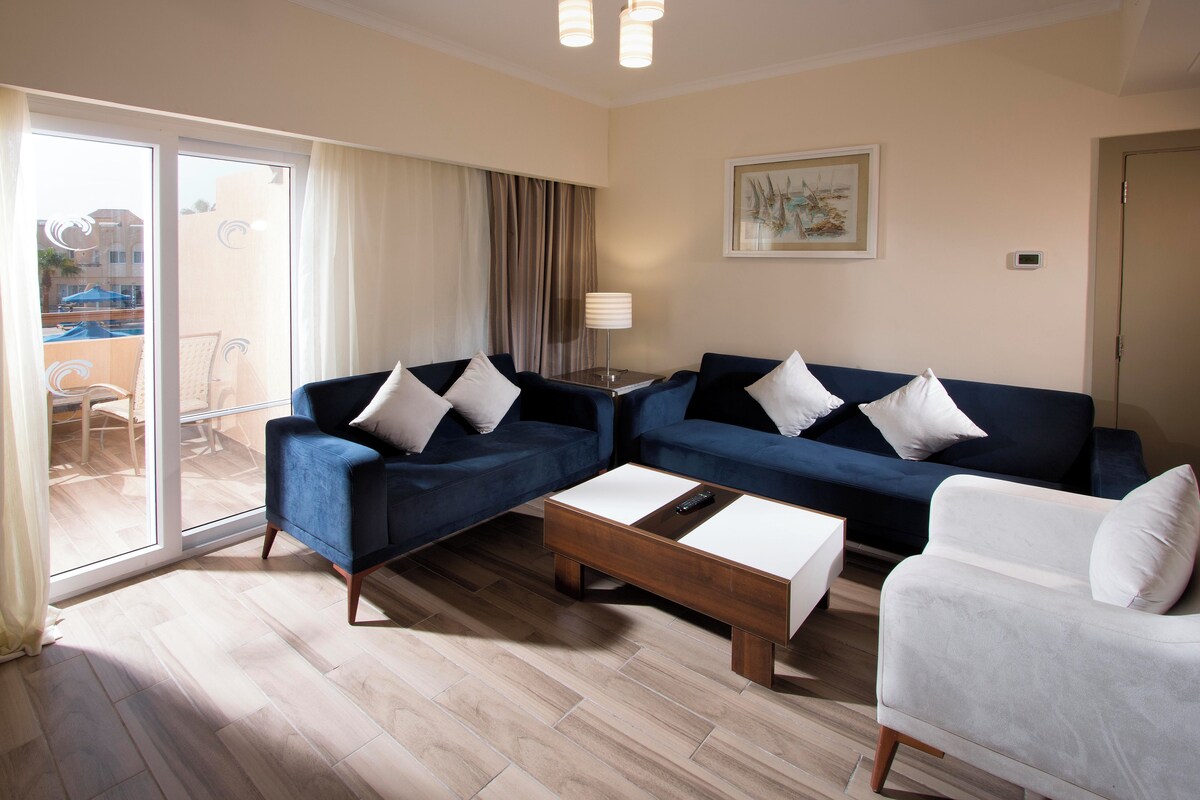 A modern living room with two blue sofas, a white armchair, and a wooden coffee table.