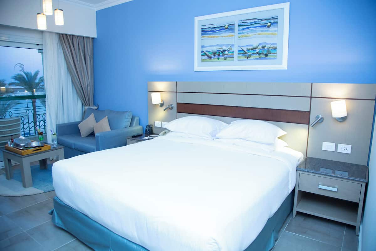 A hotel room with a large bed, a sofa, a nightstand, and a painting on the wall.