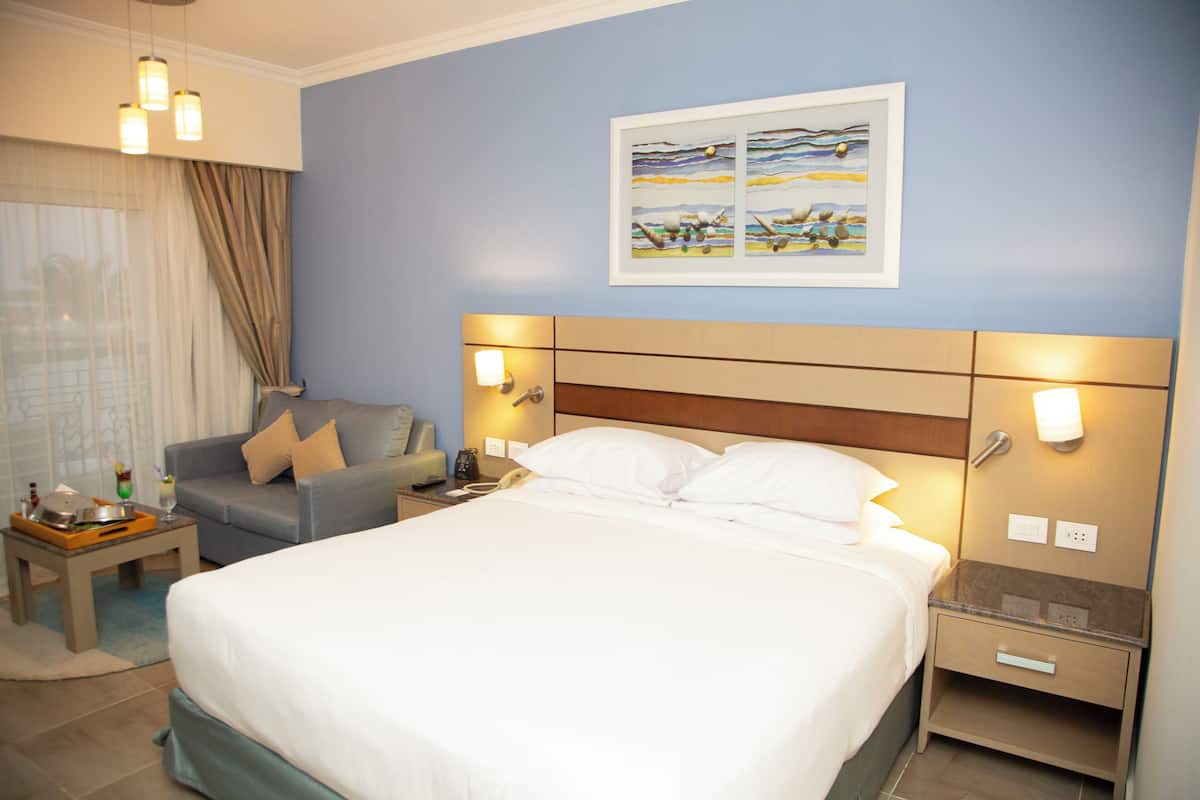 A hotel room with a large bed, a sofa, a nightstand, and a wall-mounted painting.