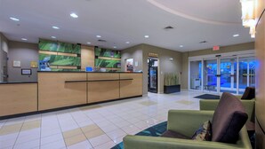 Et hotellets receptionsområde med receptionsskranke, et venteområde med grønne stole og en glasdør indgang.