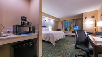 Habitación de hotel con cama, escritorio, silla, microondas, refrigerador y televisión.
