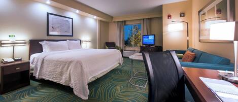 A hotel room with a bed, desk, chair, TV, and a view of the outdoors.