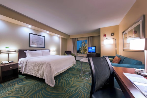 Une chambre d’hôtel équipée d’un lit, d’un bureau, d’une chaise, d’une télévision et offrant une vue sur l’extérieur.