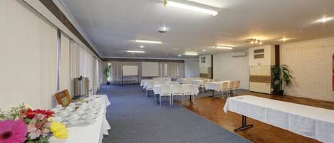 Un salón de conferencias con mesas y sillas, una estación de café y una pared de ladrillo.