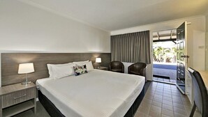 Quarto de hotel com uma cama grande, duas mesas de cabeceira com abajures, uma cadeira e vista para o exterior.