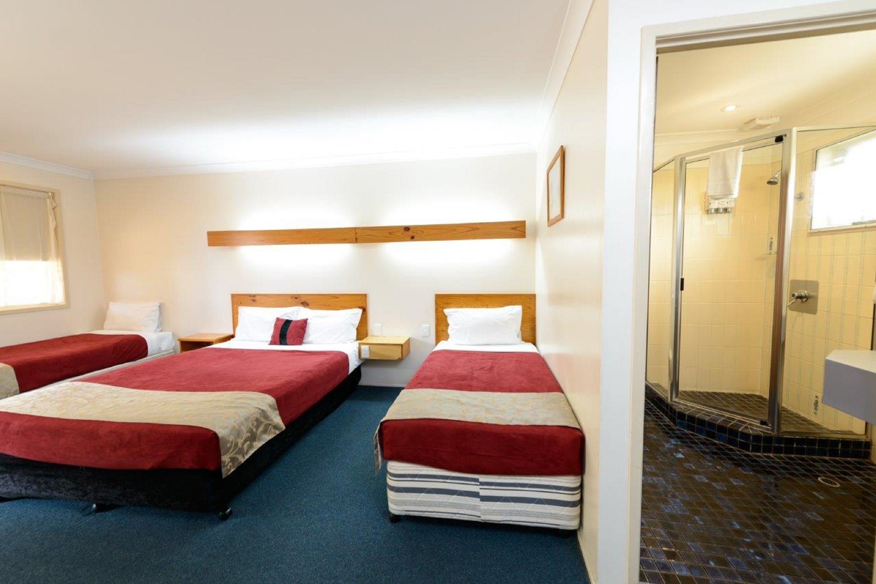 A hotel room with three beds, a shower, and a small bathroom.