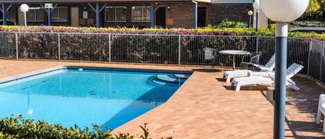 A swimming pool with lounge chairs and a covered seating area.