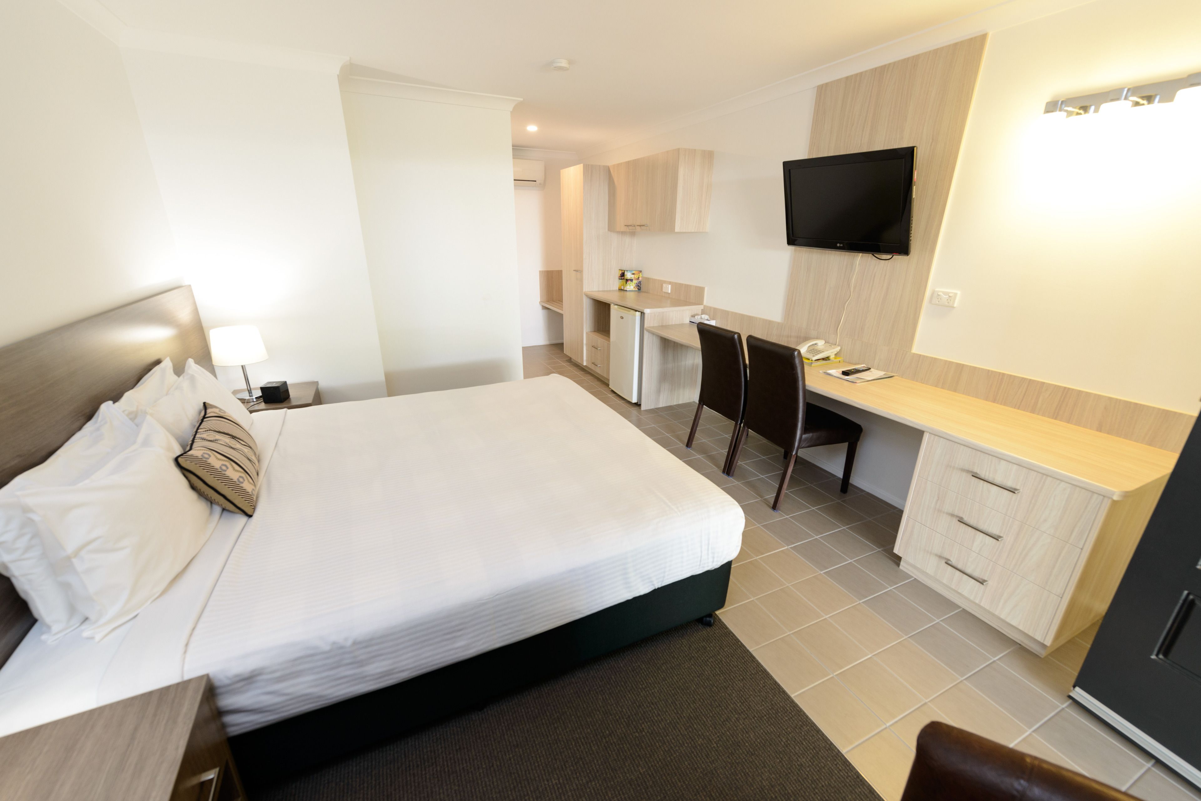 Quarto de hotel com cama, escrivaninha, cadeira, televisão e cozinha compacta.