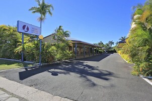 A street view of a motel with a signboard, palm trees, and a clear sky.
