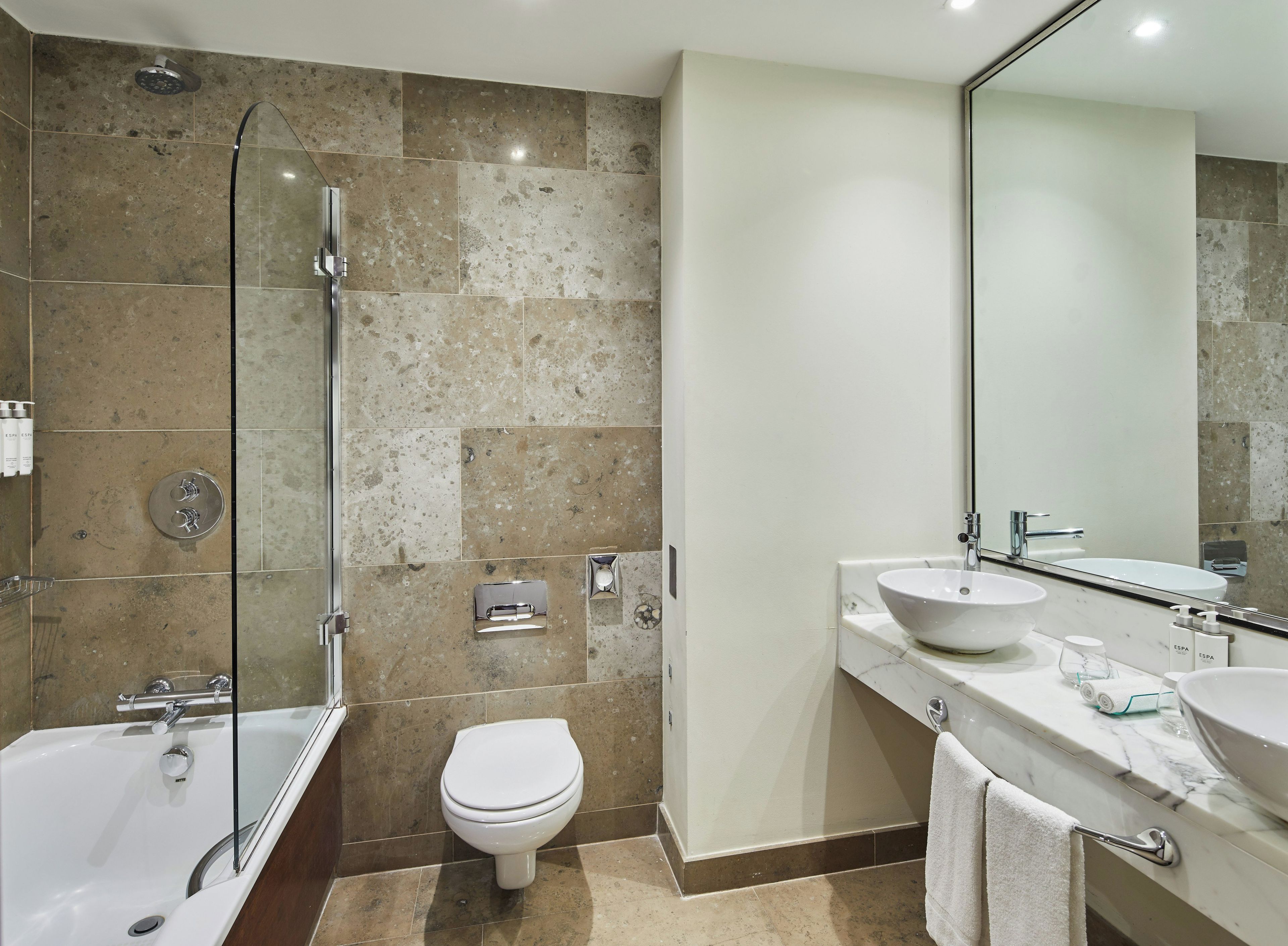 Un baño moderno con bañera, inodoro y un espejo grande.