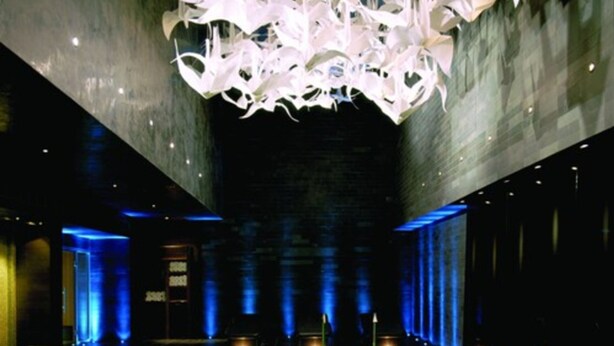 A modern interior with a geometric light installation, a central seating area, and a dark-toned floor.