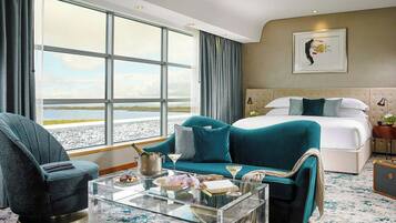 A hotel room with a large window, a bed, a sofa, a glass coffee table, and a chair.
