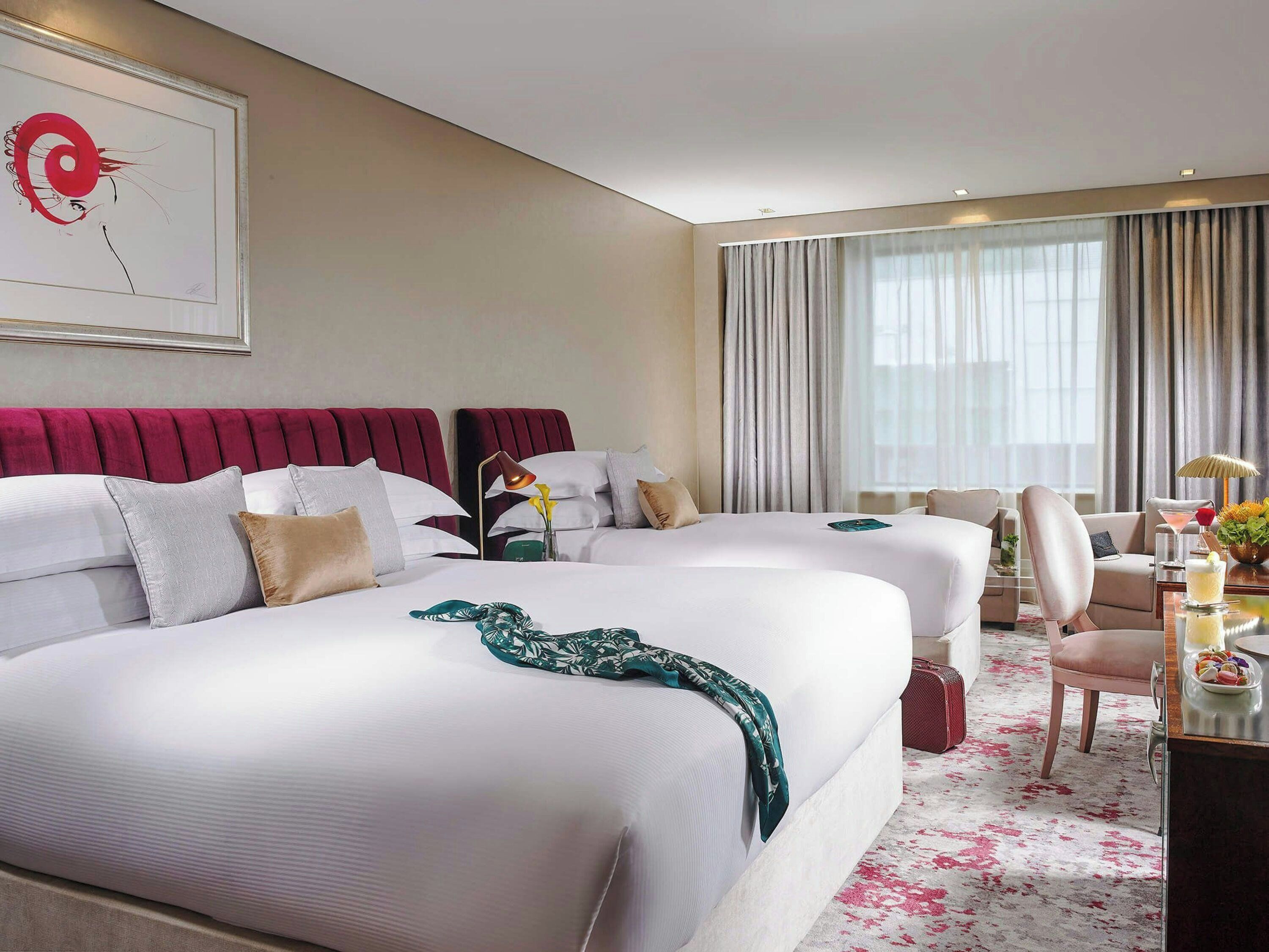Une chambre d’hôtel avec deux lits, un bureau, une chaise et une grande fenêtre avec des rideaux.