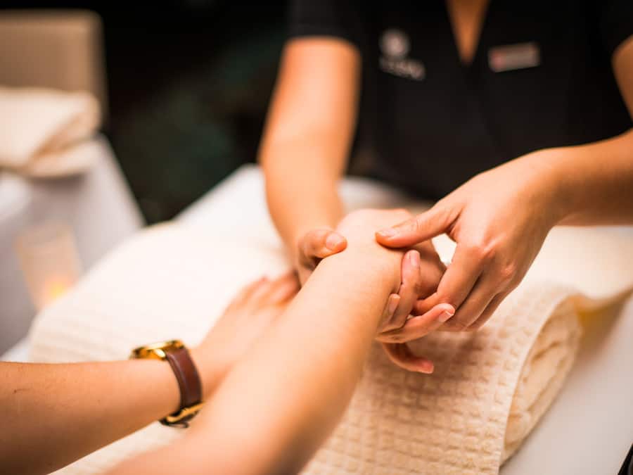 A close-up of hands being massaged, with a person wearing a gold bracelet.