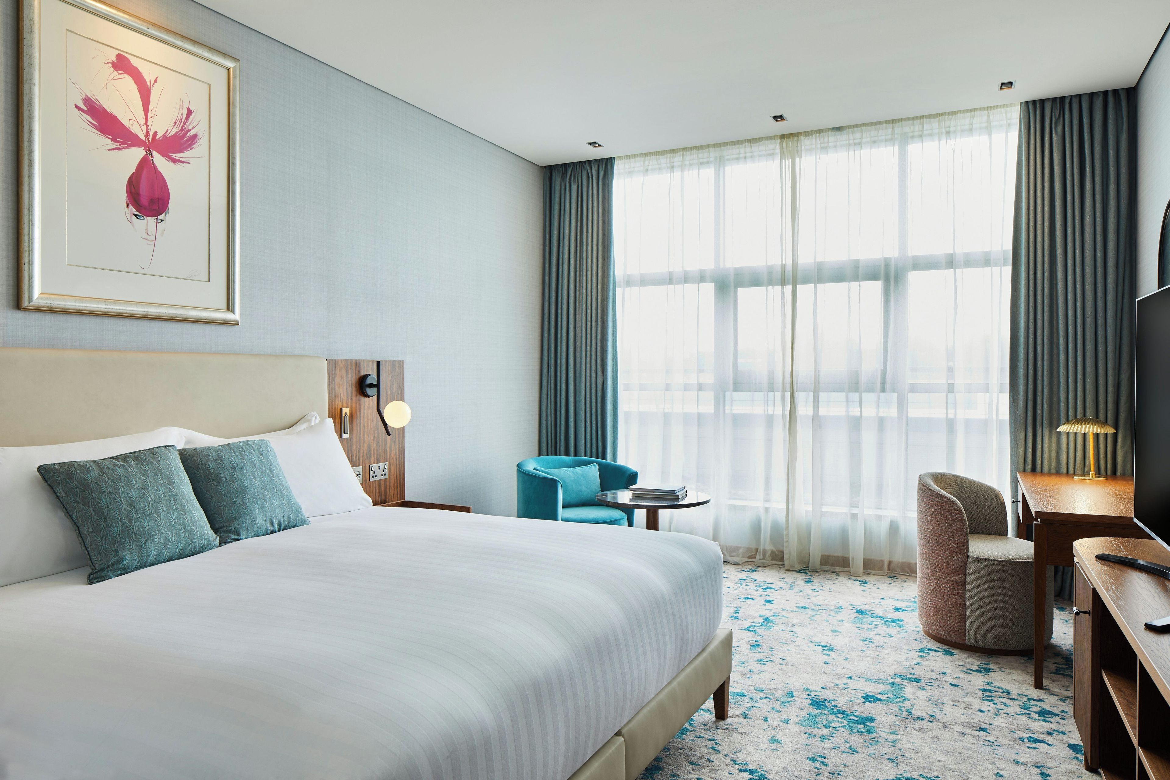 Habitación de hotel con una cama grande, un escritorio, una silla, una mesita y una ventana con cortinas.