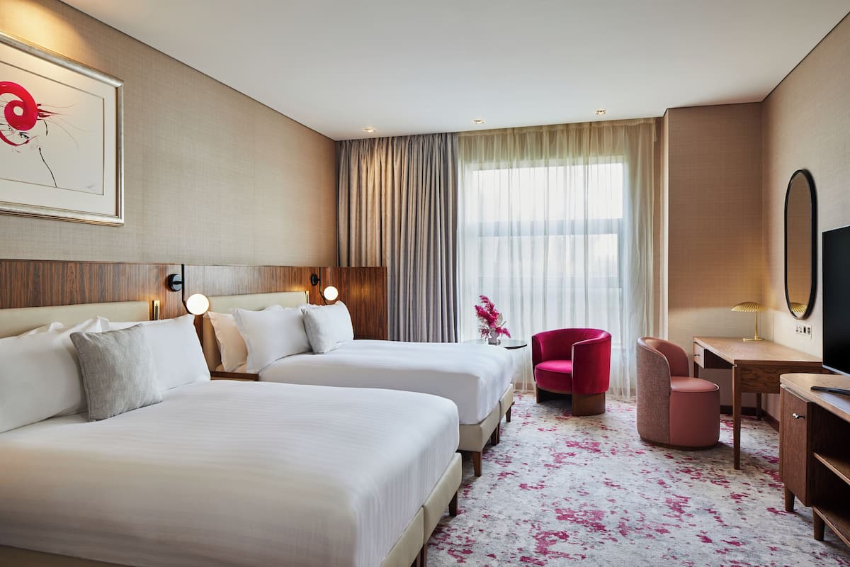 Een hotelkamer met twee bedden, een bureau, een stoel, een televisie en een groot raam met gordijnen.