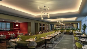 A modern restaurant with green seating, a bar area, and a well-lit ceiling.