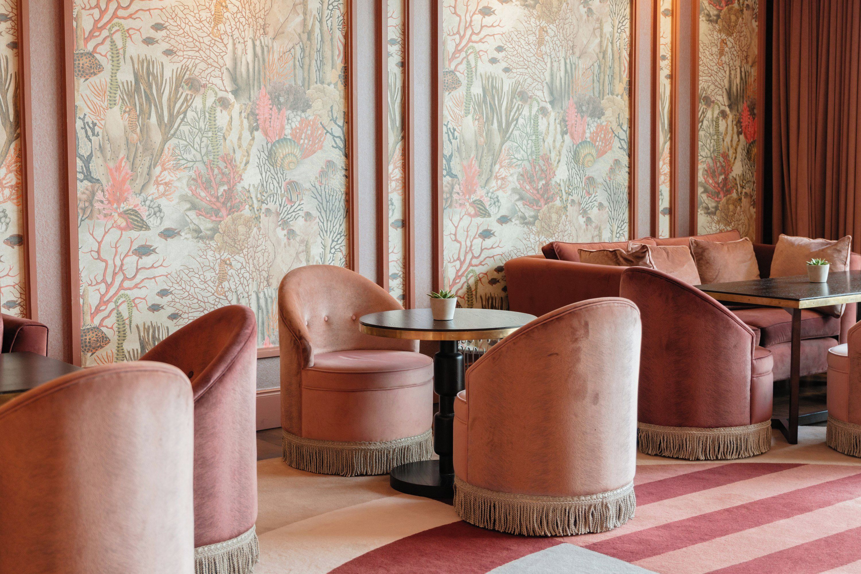A restaurant interior with round tables and cushioned chairs, a patterned wallpaper, and a striped carpet.