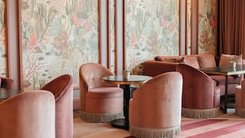 A restaurant interior with round tables and cushioned chairs, a patterned wallpaper, and a striped carpet.