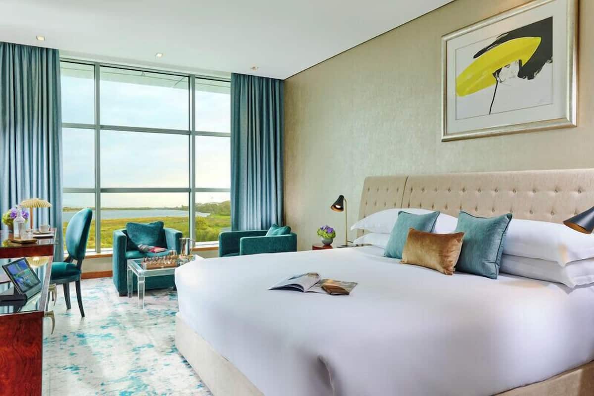 Een hotelkamer met een groot bed, een bureau met een laptop, een stoel en uitzicht op het omliggende landschap.