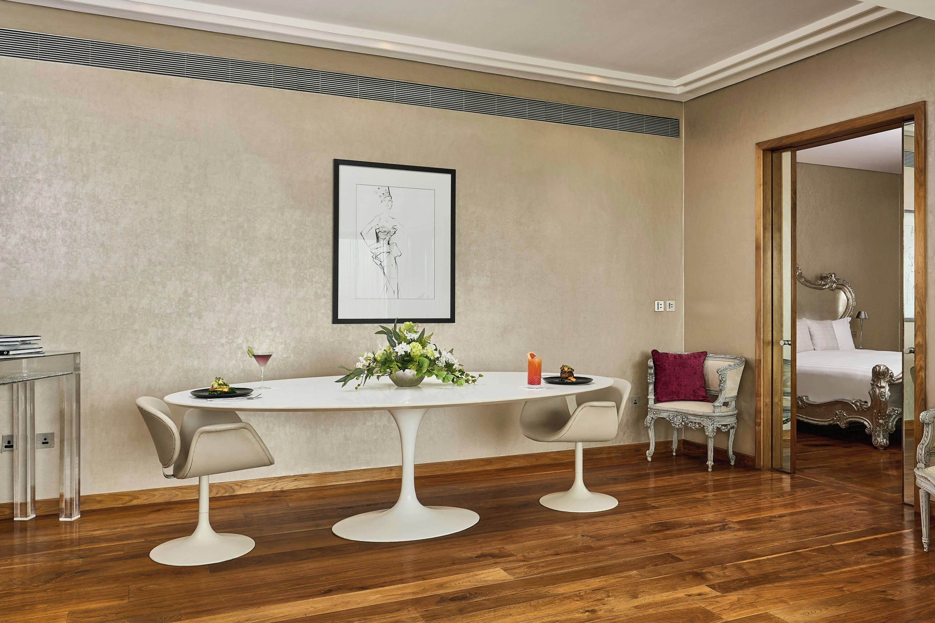 Un comedor con una mesa blanca, dos sillas, una obra de arte enmarcada en la pared y piso de madera.