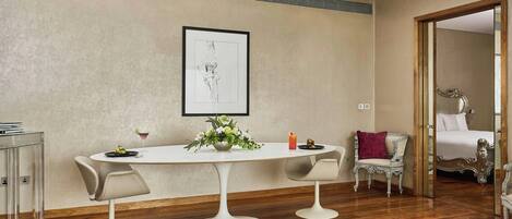 Un comedor con una mesa blanca, dos sillas, una obra de arte enmarcada en la pared y piso de madera.