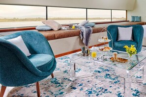 A modern living area with two teal armchairs, a glass coffee table, and a view of the ocean through large windows. - The G Hotel and Spa (Galway)