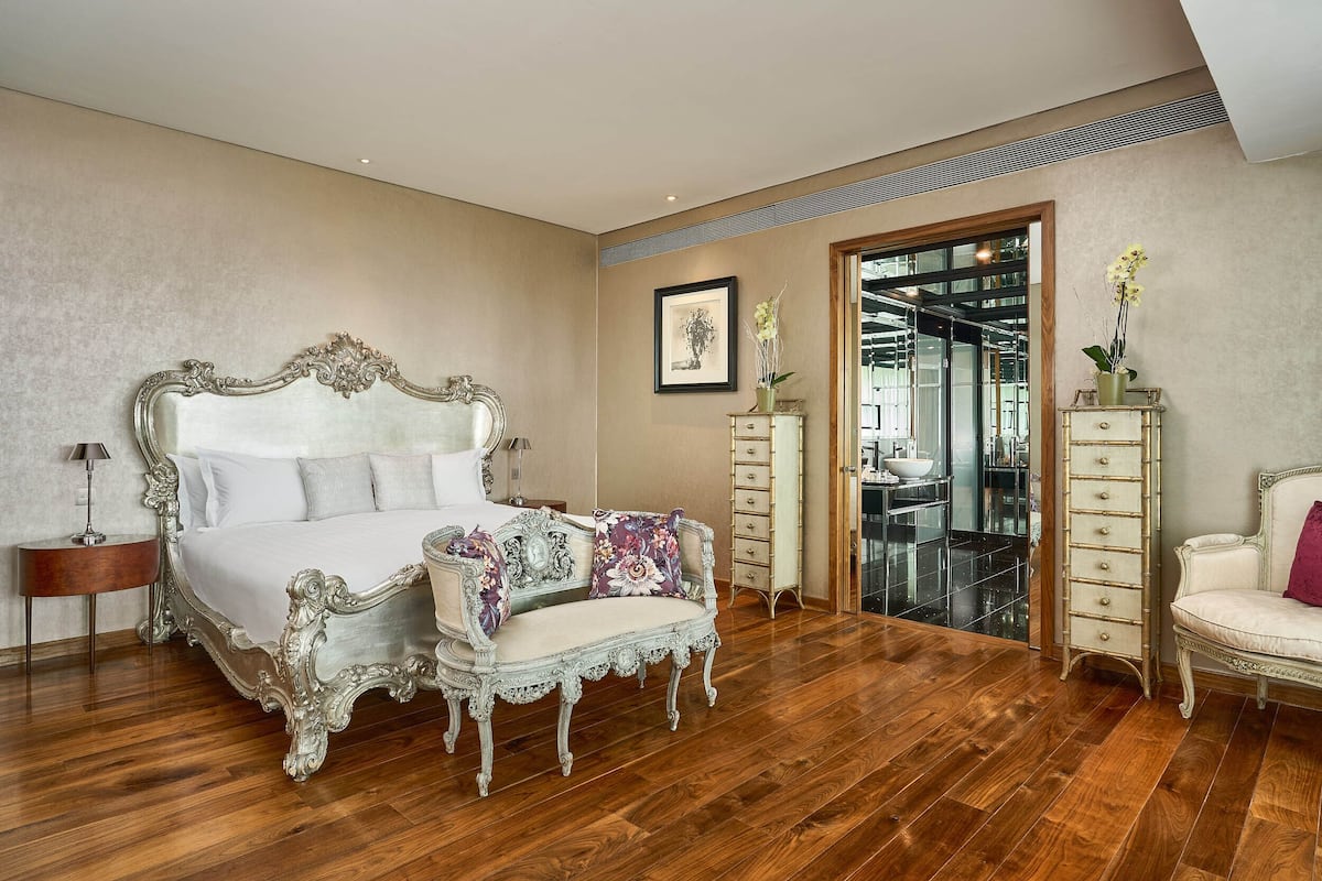 Een slaapkamer met een groot, versierd bed, een chaise longue, een kaptafel en een stoel.