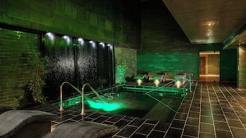 A spa area with a hot tub, seating, and a wall with water features.