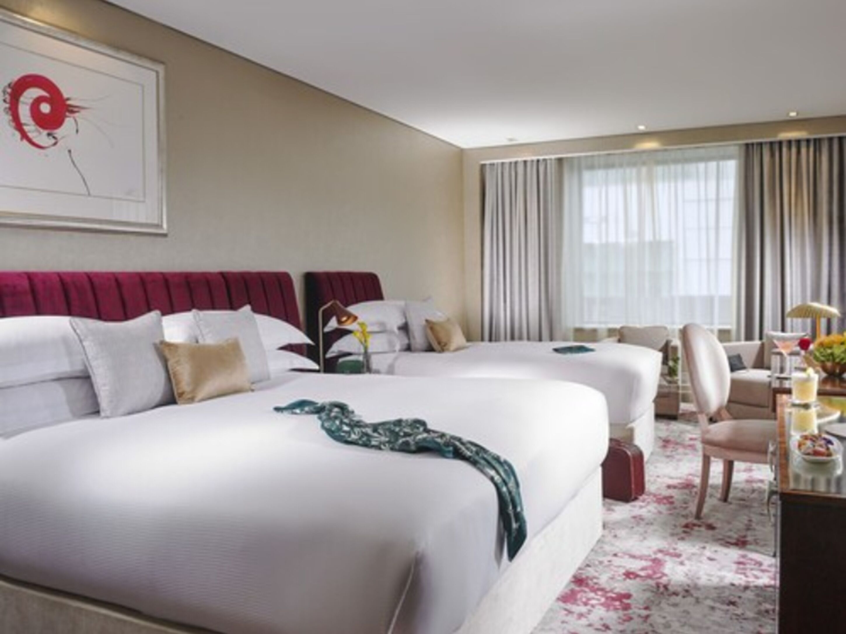 Une chambre d’hôtel avec deux lits, un bureau, une chaise et une grande fenêtre avec des rideaux.