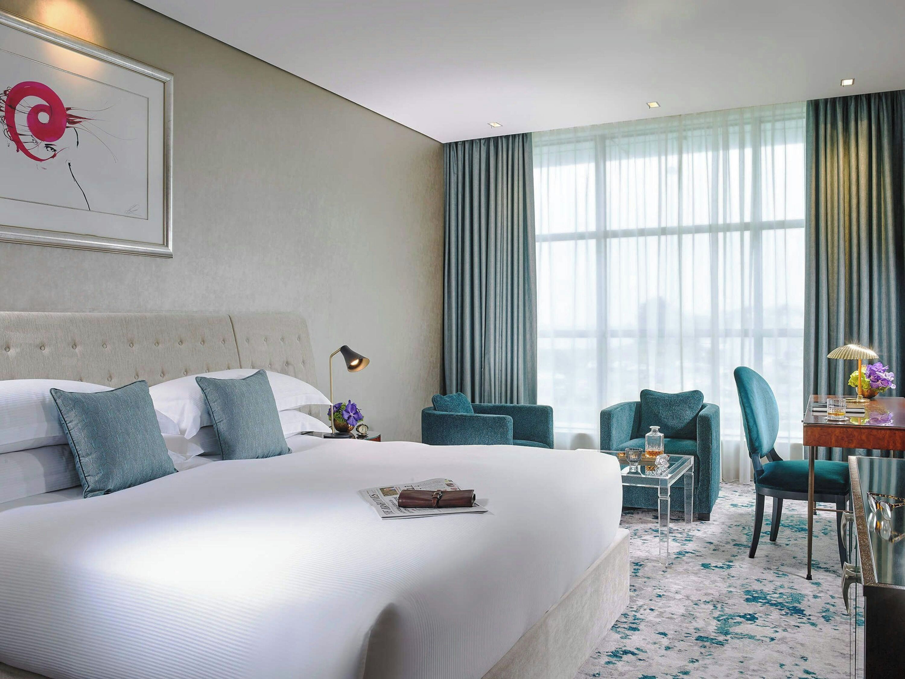 Habitación de hotel con una cama grande, dos sillas, una mesita y una ventana con cortinas.