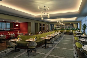 A restaurant with a bar area, green upholstered seating, and a patterned floor. - The G Hotel and Spa (Galway)