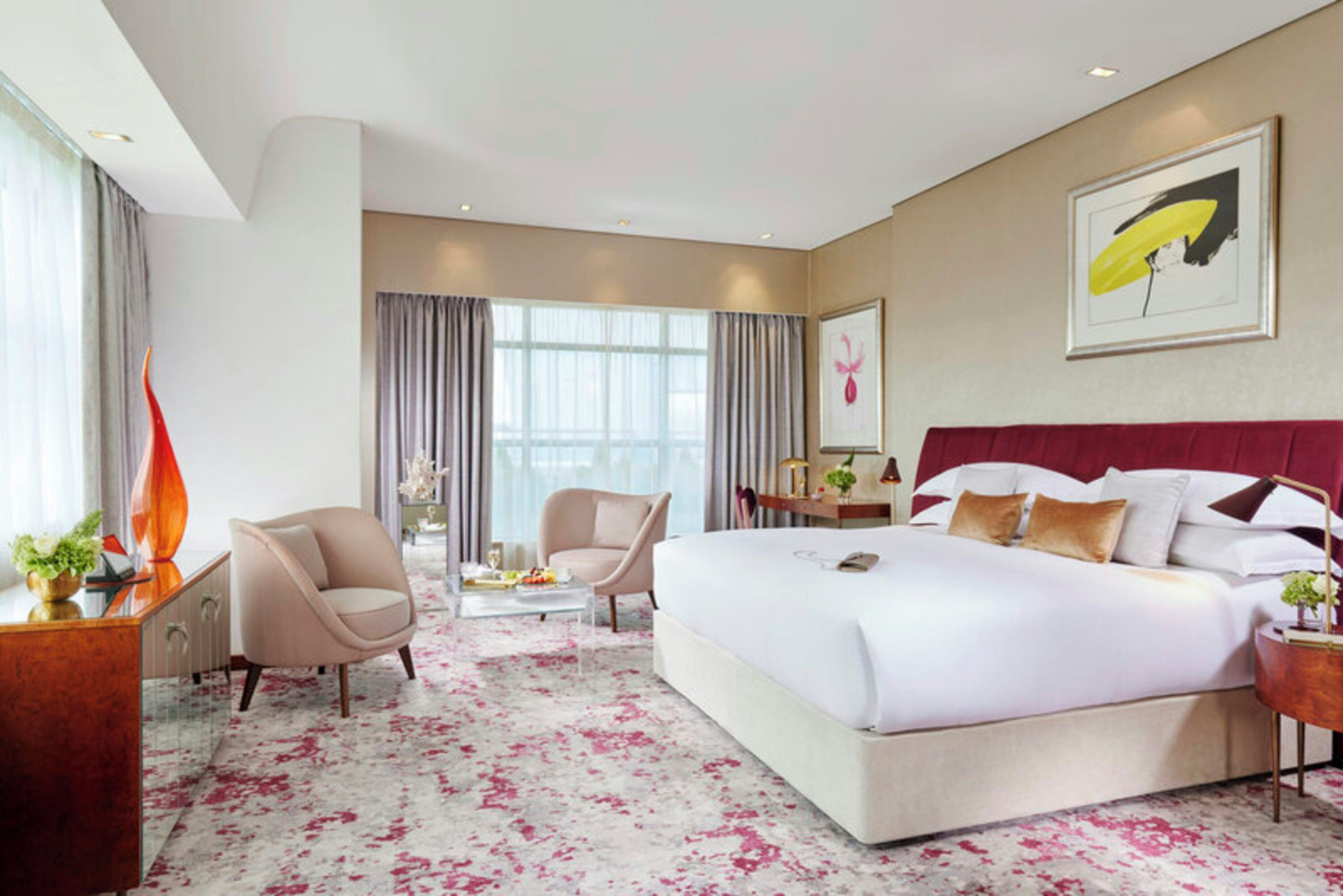Una habitación de hotel con una cama grande, dos sillones, un escritorio y un ventanal amplio.