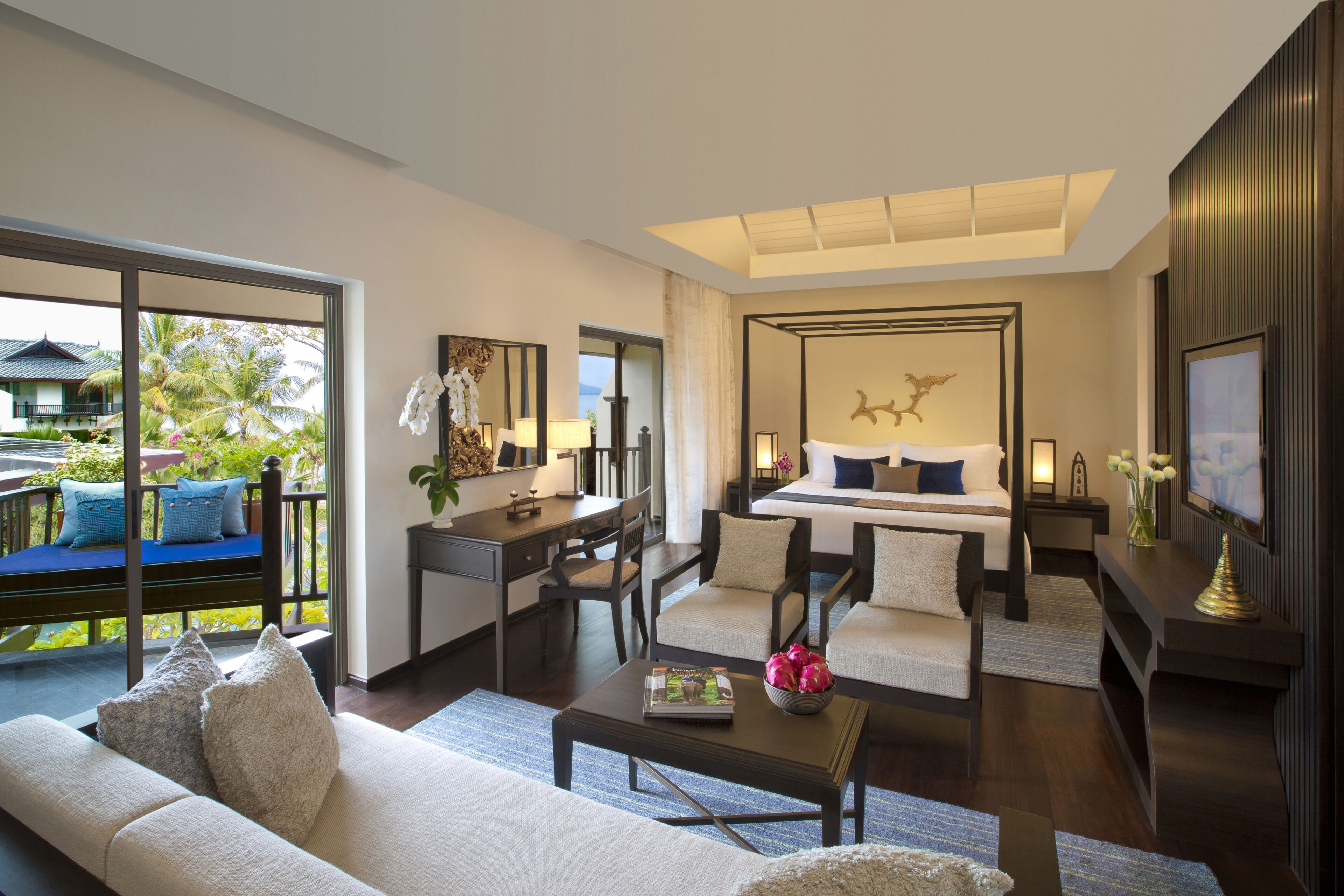 A modern hotel room with a balcony, a bed with a headboard, a desk, a sofa, and a television.