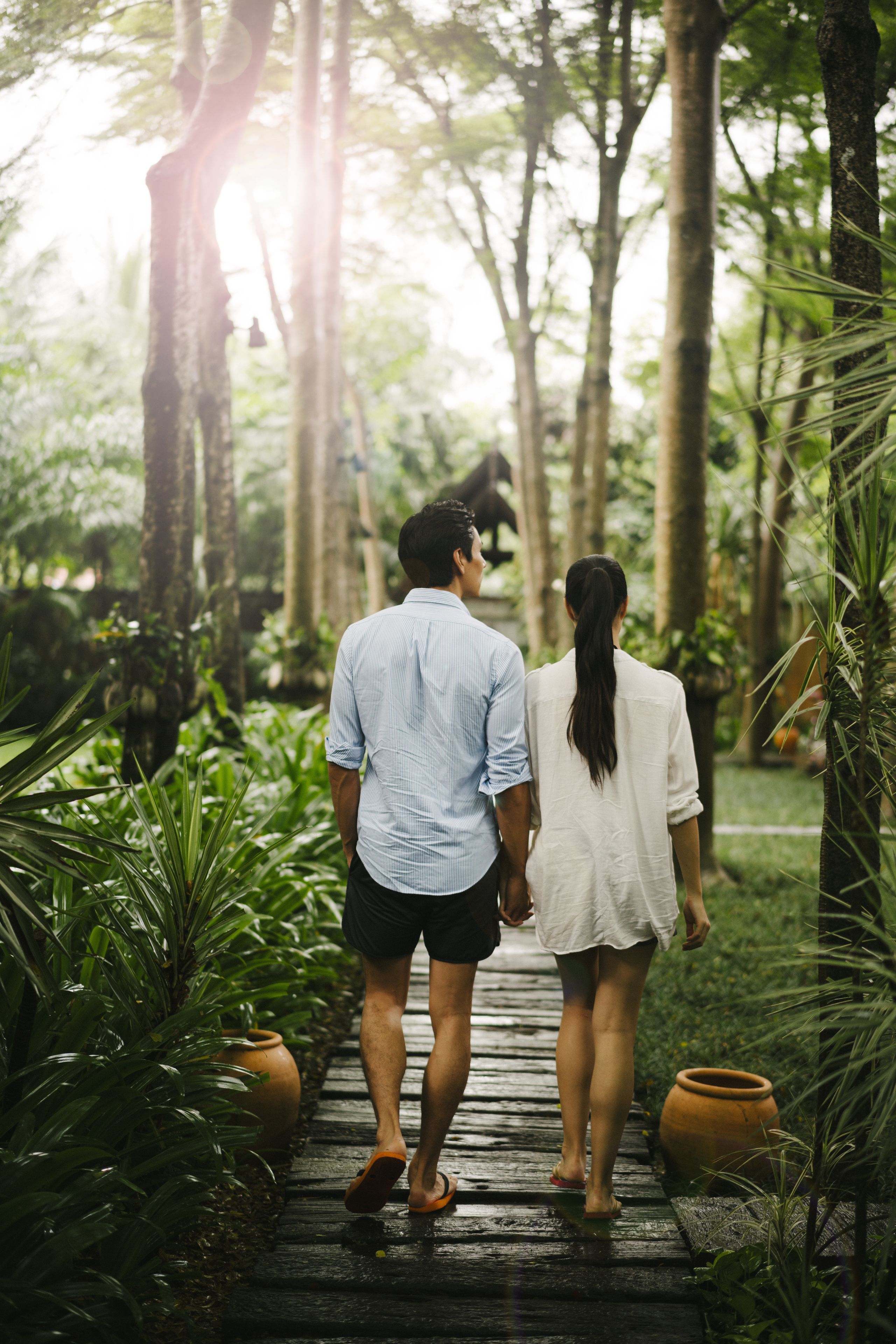 Una pareja caminando por un sendero de madera rodeado de abundante vegetación y altos árboles.
