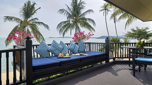 A balcony with a sofa, pillows, and a table with a book and a tray. - Anantara Bophut Koh Samui Resort (Koh Samui)