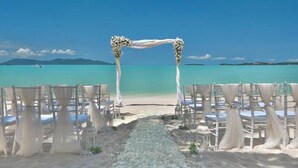 Decoración para una boda en la playa, con un arco blanco y sillas dispuestas para los invitados.